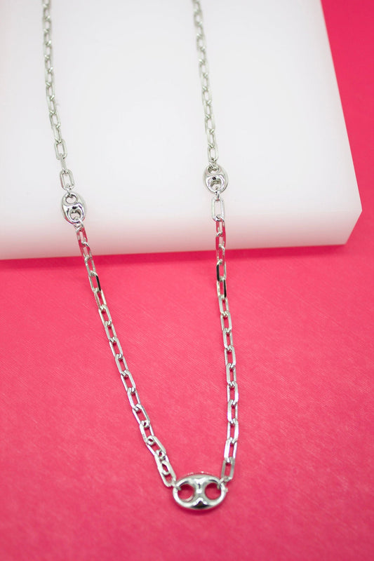 A shiny silver link necklace rests against a vibrant pink and white background.
