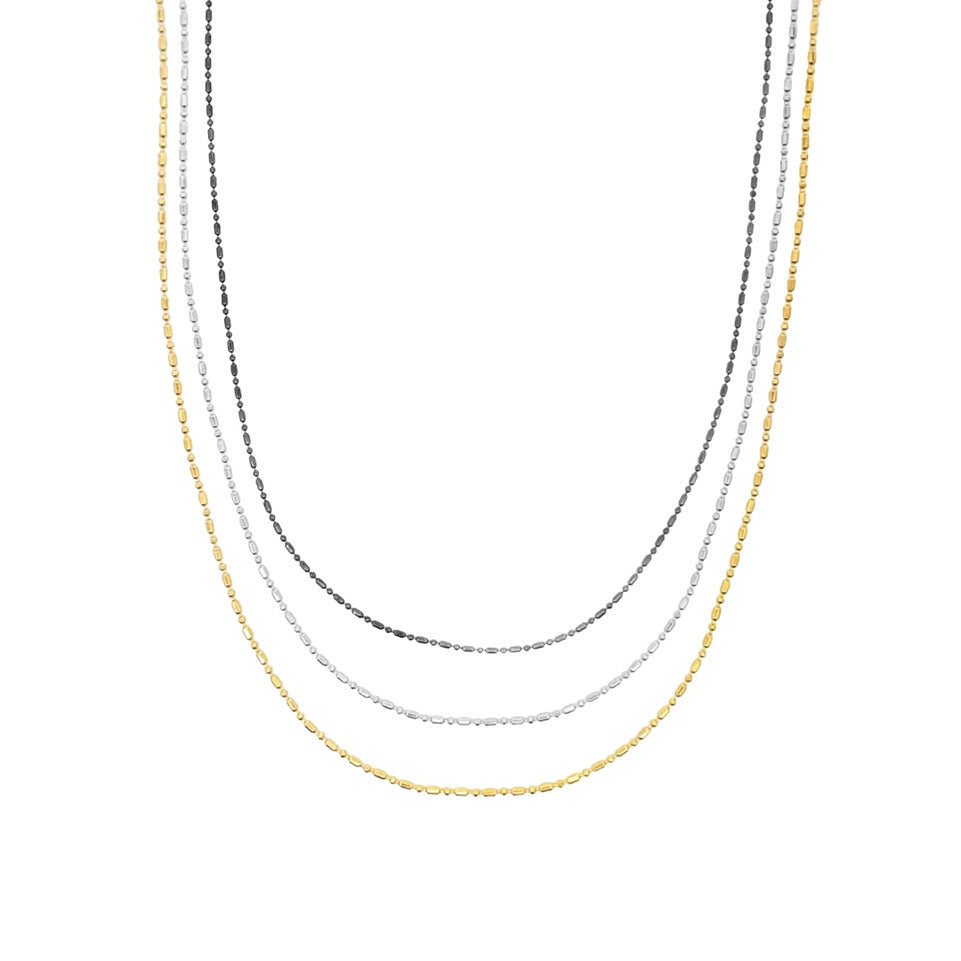Three delicate layered necklaces in yellow gold, white gold, and black metal drape gracefully.