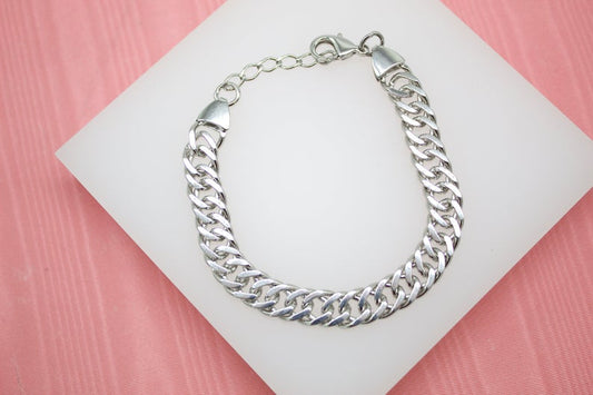 A silver cuban link chain bracelet rests on a white display stand against a pink background.