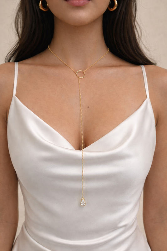 A woman wearing a gold lariat necklace and matching hoop earrings showcases the delicate jewelry against a white satin dress.