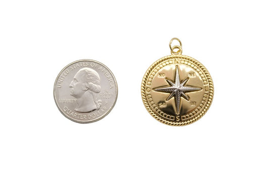 A gold compass pendant rests next to a US quarter coin to display its size.