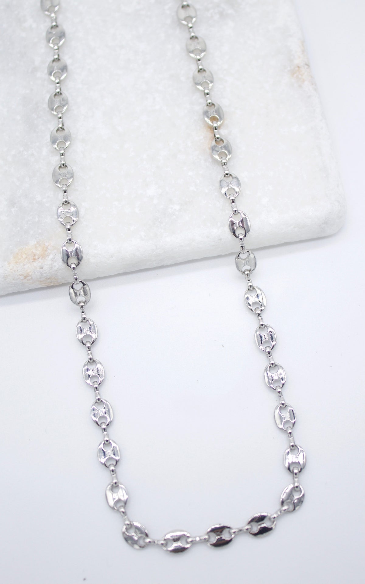 A shiny silver puff mariner link chain necklace rests on a white marble background.