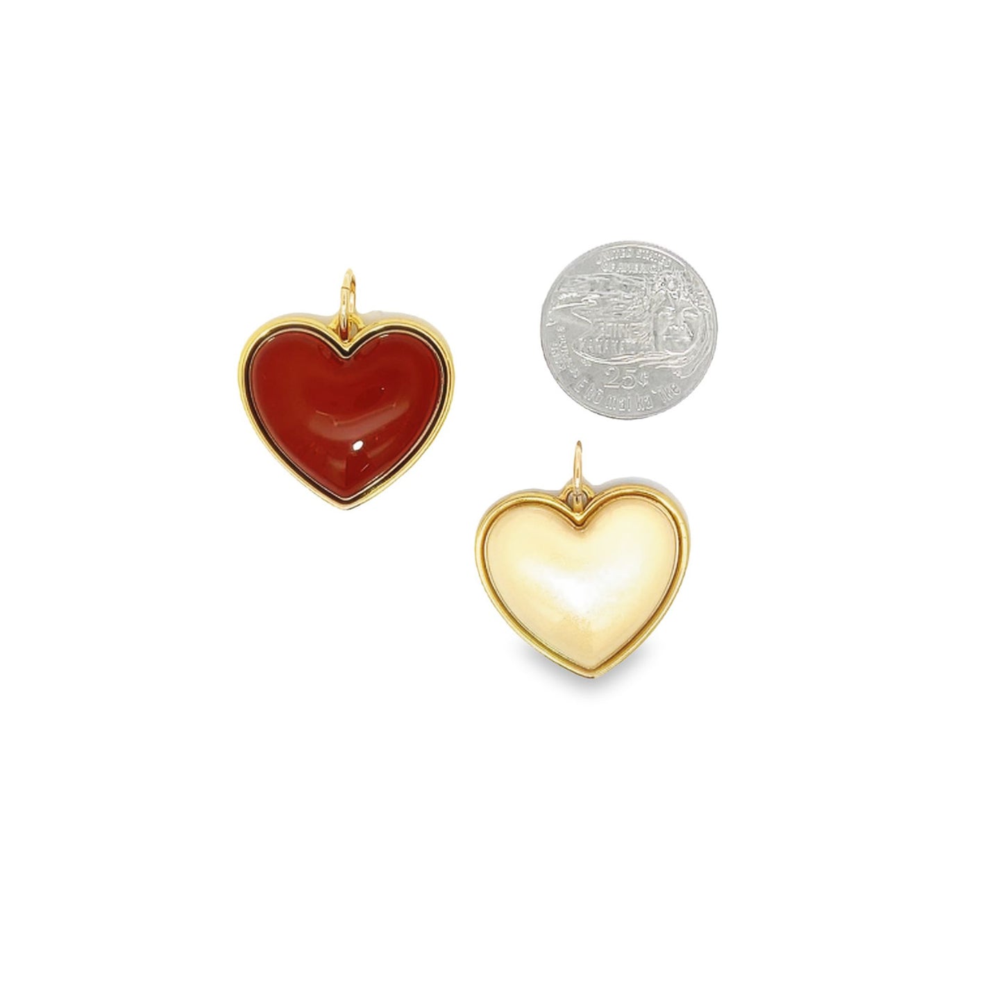 Two gold heart-shaped pendants, one red carnelian and one creamy white, rest next to a US quarter coin for scale on a white background.