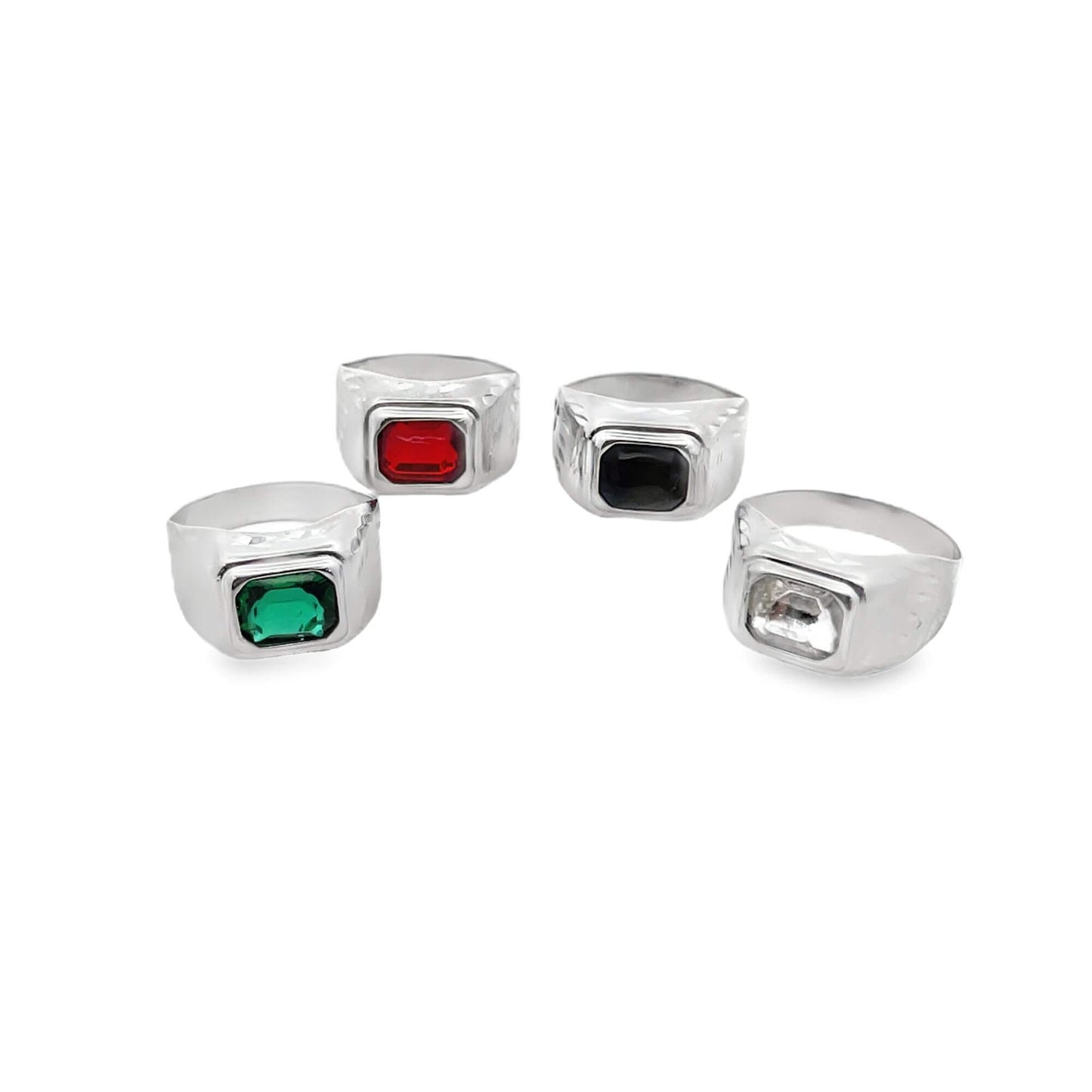 Four silver signet rings featuring emerald-cut green, red, black, and clear gemstones display on a white surface.