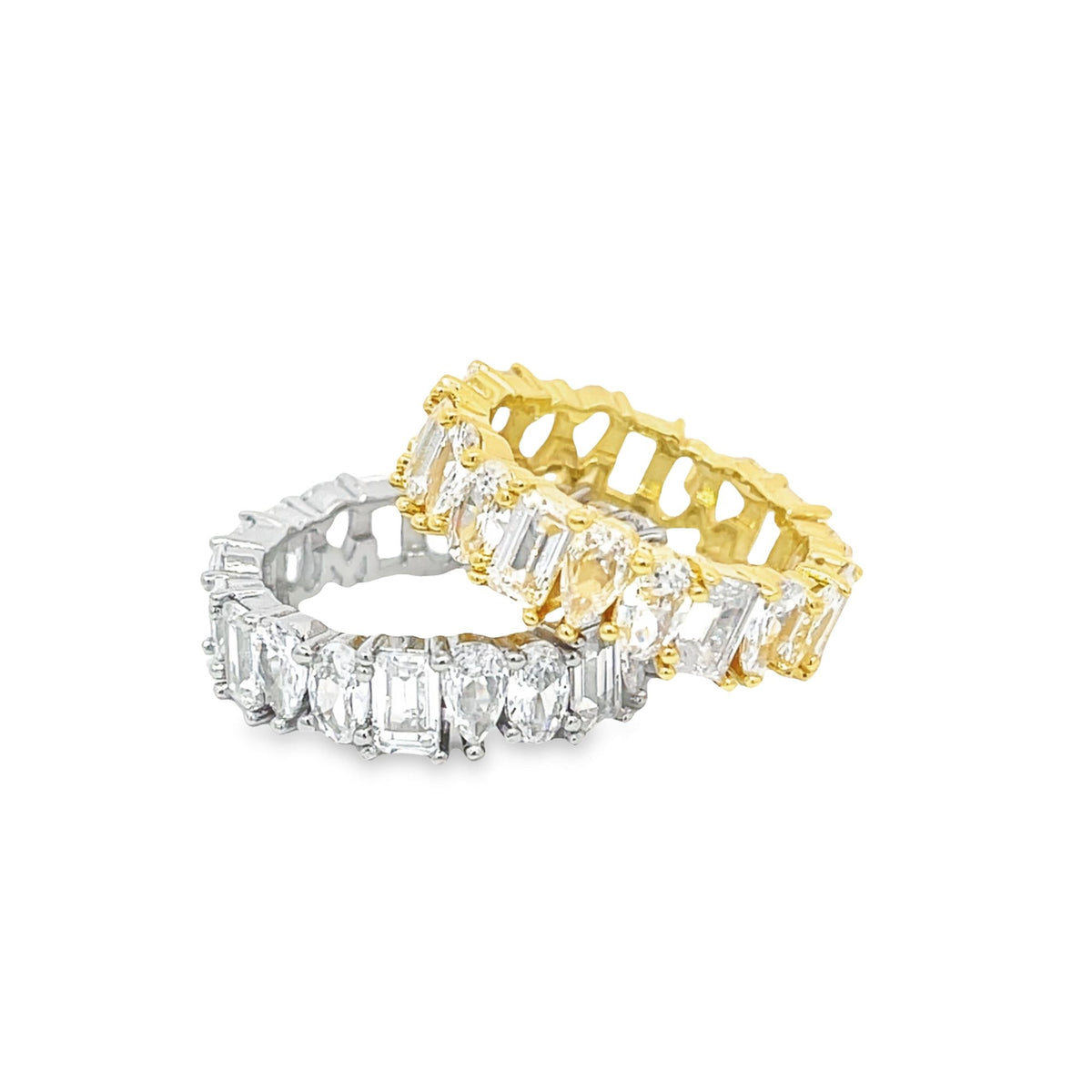 Two interlocking eternity bands featuring alternating emerald and pear-cut cubic zirconia stones sparkle against a white background, with one band in polished silver and the other in gold.