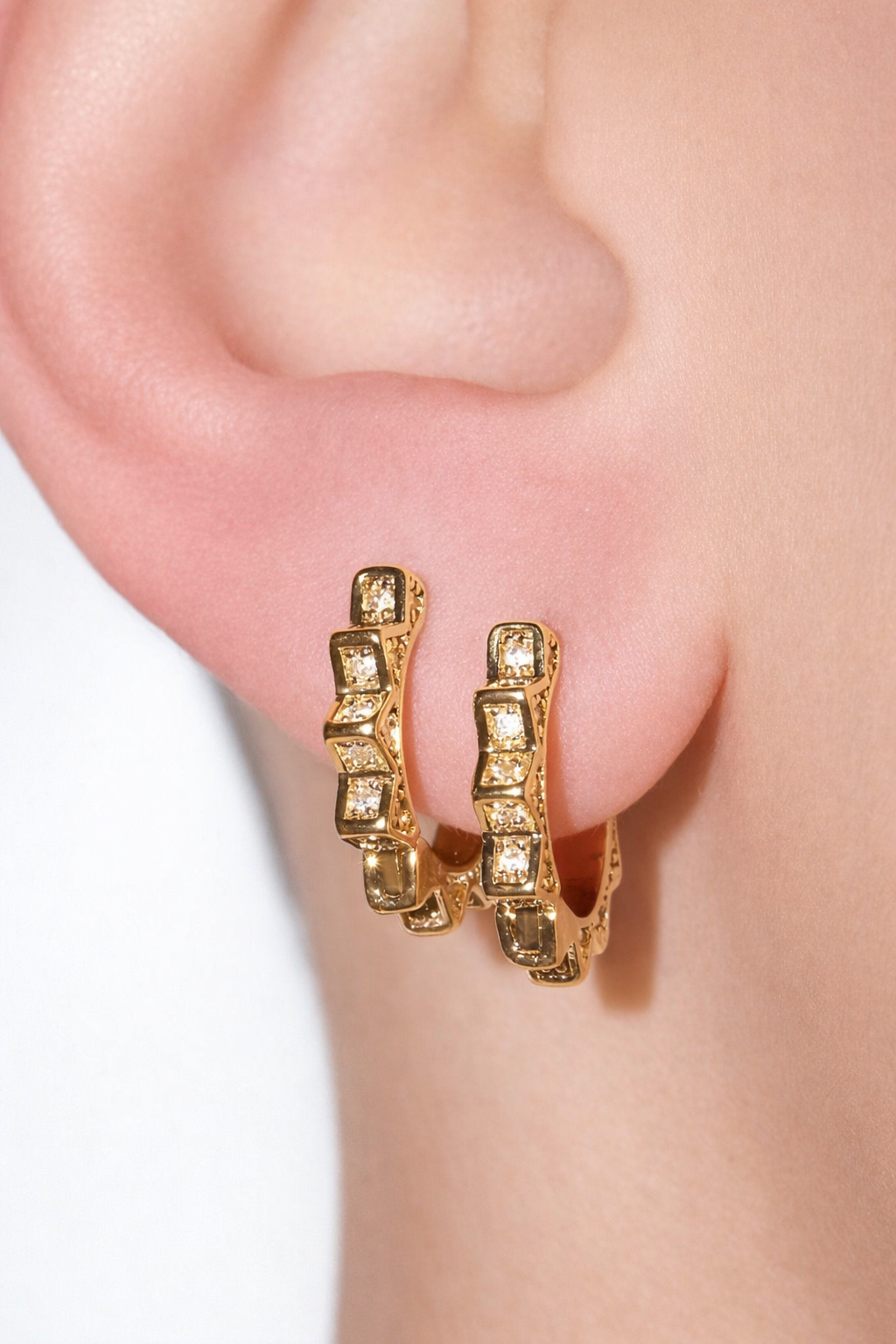 A close-up shot showcases a person wearing unique geometric gold hoop earrings embedded with sparkling crystals.