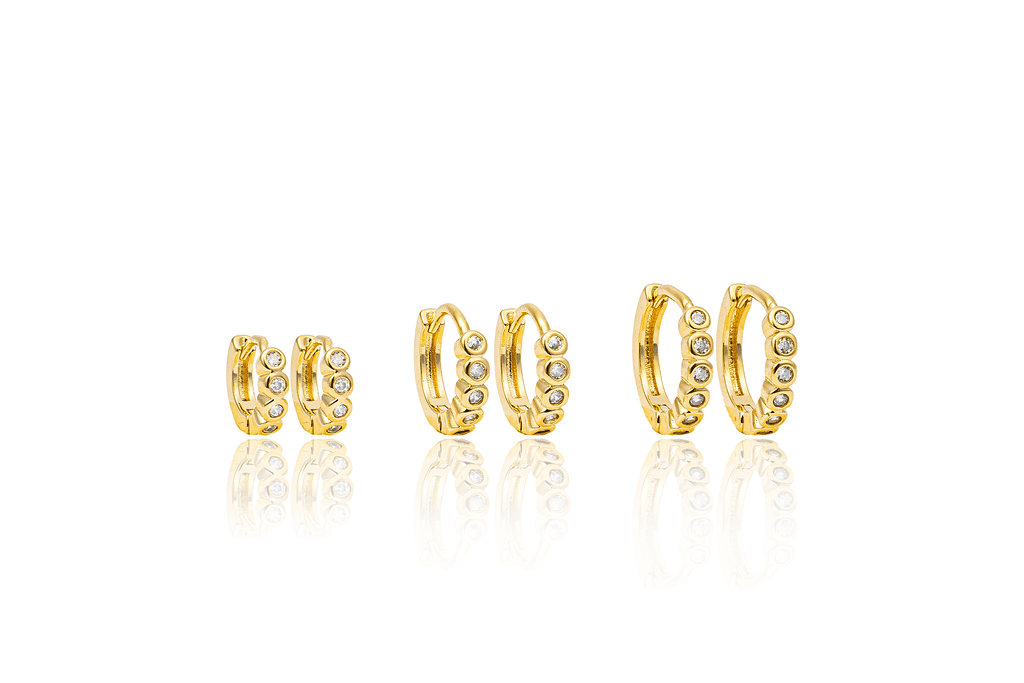 Three pairs of gold huggie hoop earrings featuring sparkling bezel-set diamonds display in graduating sizes against a clean white background.
