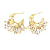 A pair of hammered gold crescent hoop earrings dangling delicate white pearls against a plain white background.
