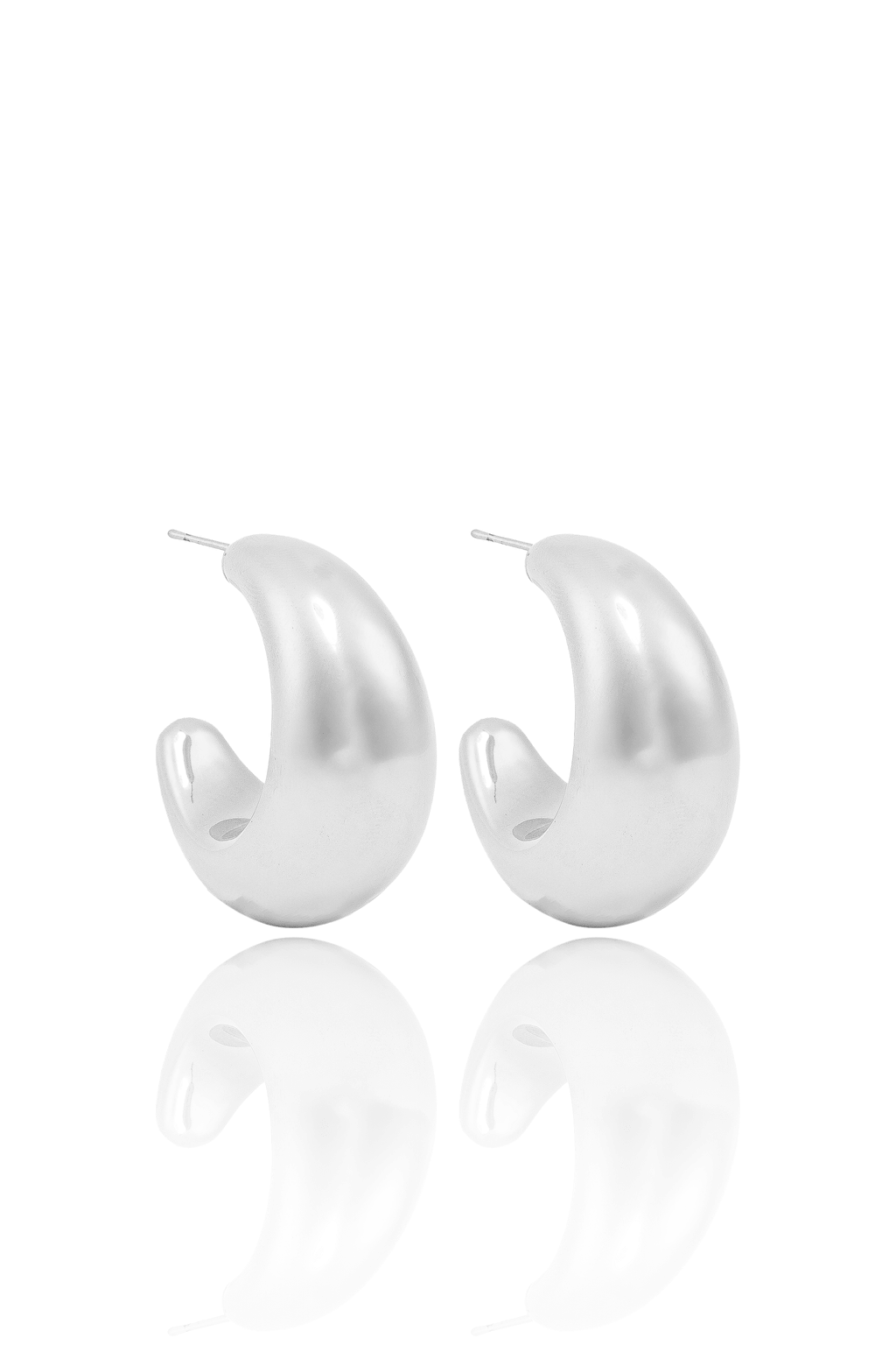 A pair of thick, polished silver hoop earrings rest on a white surface with their reflections visible below.