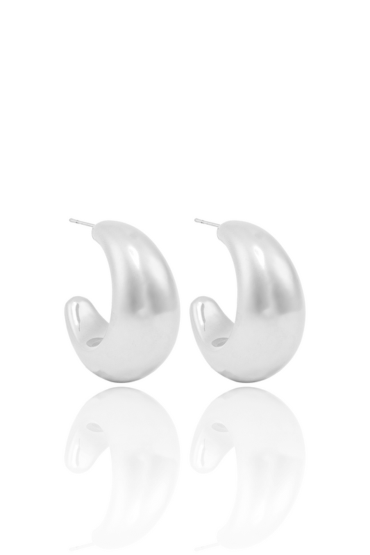 A pair of thick, polished silver hoop earrings rest on a white surface with their reflections visible below.