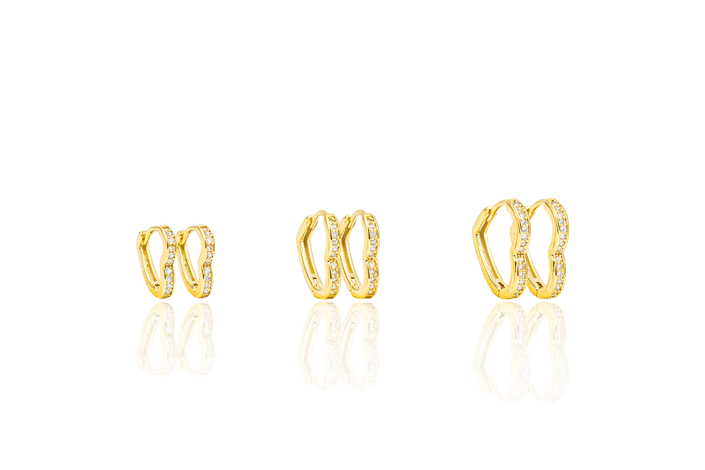 Three pairs of gold heart-shaped hoop earrings with sparkling cubic zirconia stones display their reflections on a clean white surface.