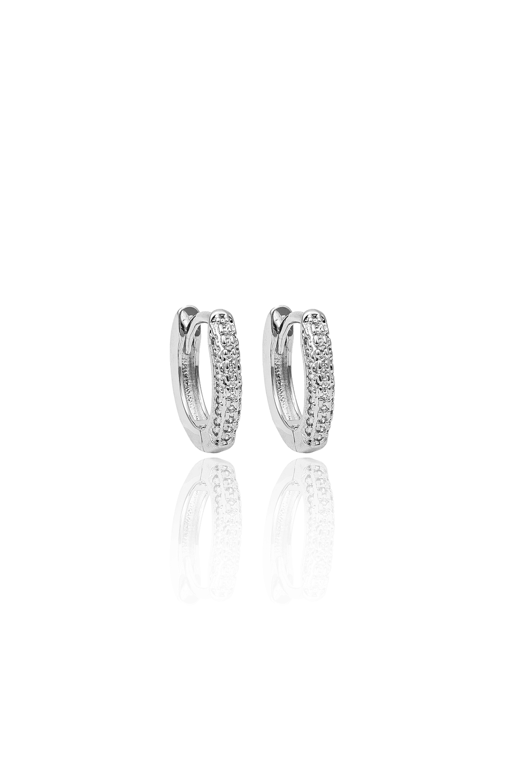 A pair of silver huggie hoop earrings embedded with small sparkling diamonds gleams against a white background.