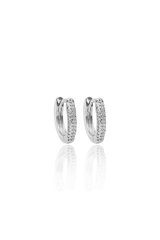 A pair of silver huggie hoop earrings embedded with small sparkling diamonds gleams against a white background.