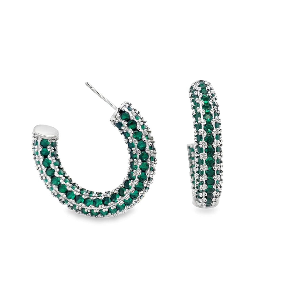 A pair of silver hoop earrings paved with sparkling green cubic zirconia stones gleams against a white background.