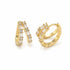 A pair of gold huggie hoop earrings adorned with sparkling baguette and round cubic zirconia stones rests against a plain white background.