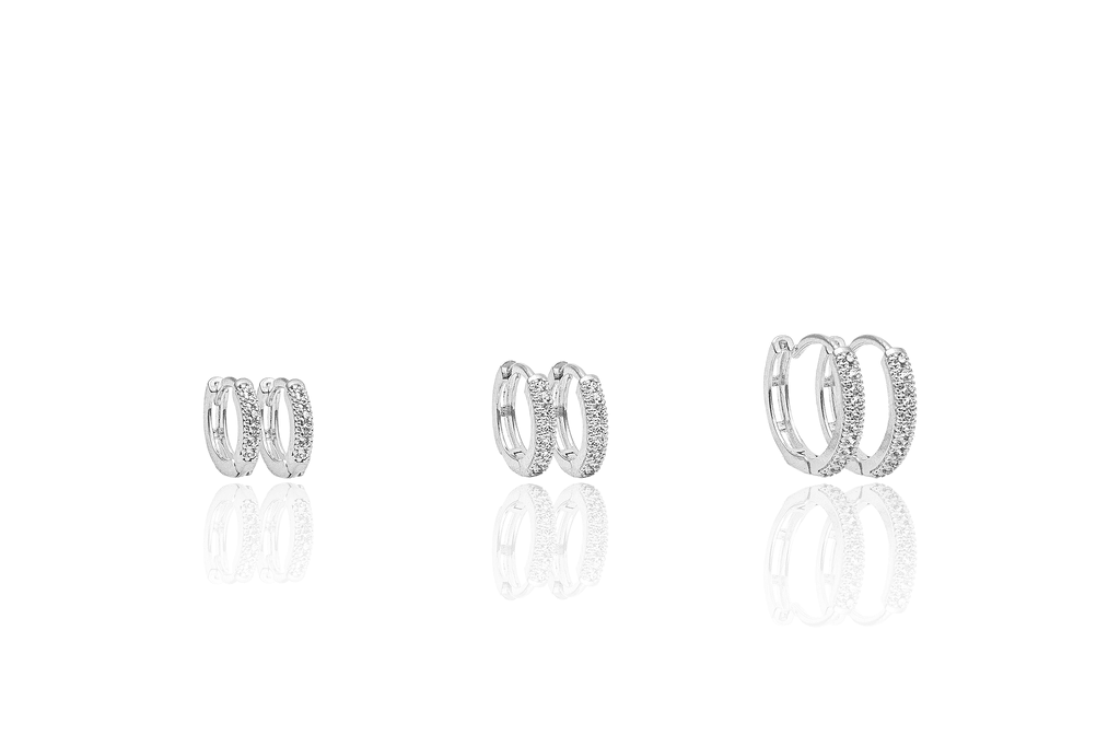 Three pairs of pavé-set diamond huggie hoop earrings in ascending sizes rest on a reflective white surface.