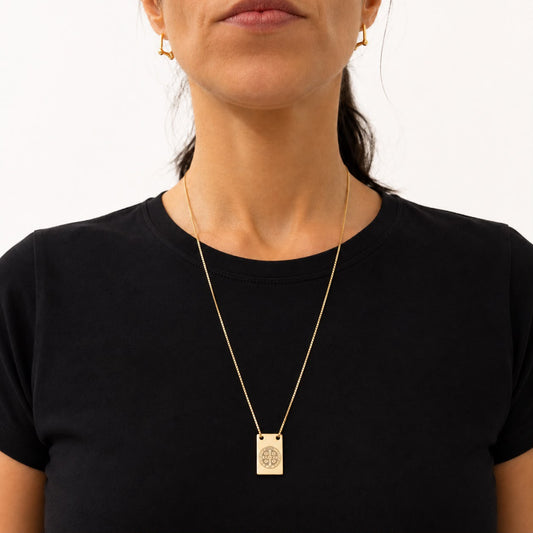 A woman wearing a black t-shirt models a gold St. Benedict medallion pendant necklace and matching small hoop earrings.