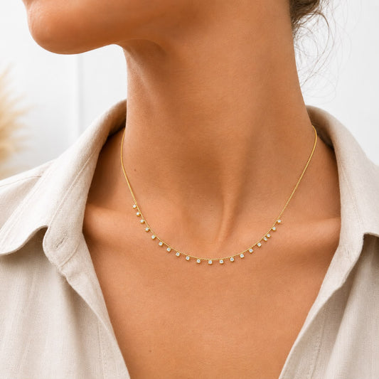 A woman wears a delicate gold chain necklace sparkling with evenly spaced diamond station stones.