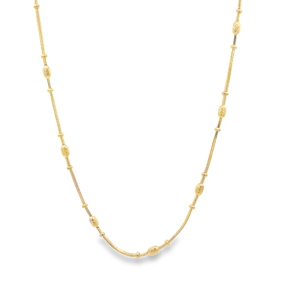 A delicate gold chain necklace drapes gracefully against a plain white background, featuring evenly spaced textured beads along its length.
