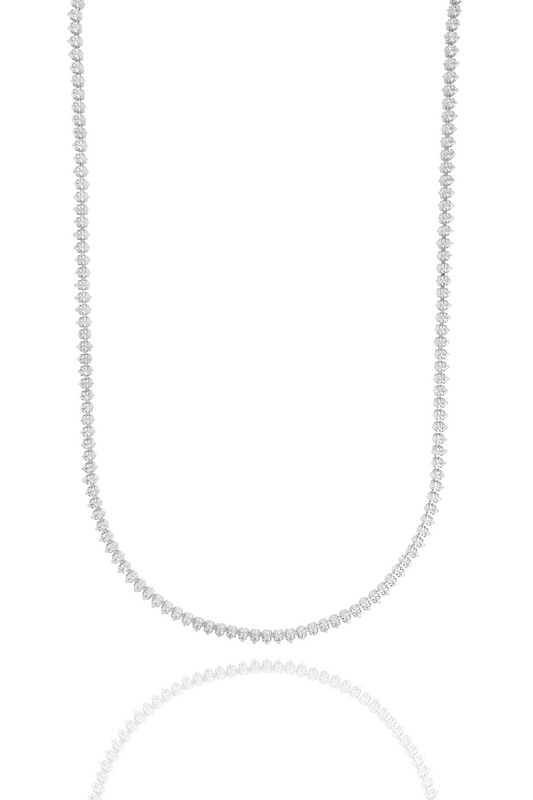 A sparkling diamond tennis necklace drapes gracefully against a clean white background, reflecting softly below.