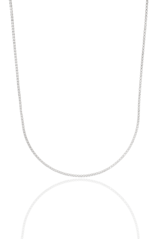 A sparkling diamond tennis necklace drapes elegantly against a clean white background, reflecting softly below.
