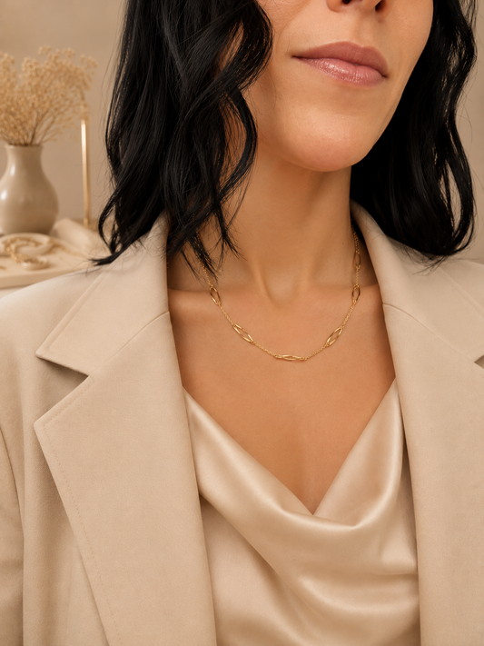 A woman with dark hair wearing a beige blazer and satin top showcases an elegant gold link chain necklace.