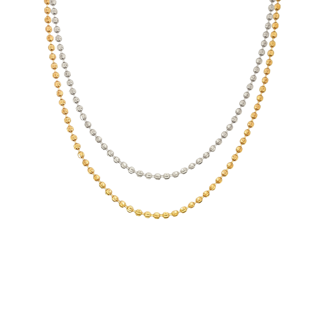 Two delicate layered ball chain necklaces, one in silver and one in gold, drape gracefully against a white background.