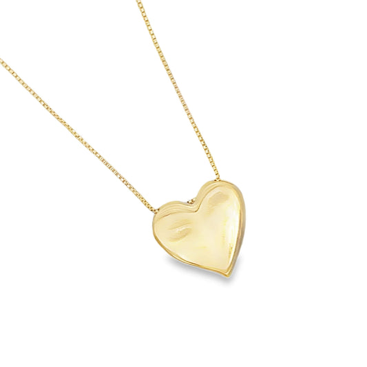 A polished gold heart pendant hangs delicately from a fine chain necklace against a white background.