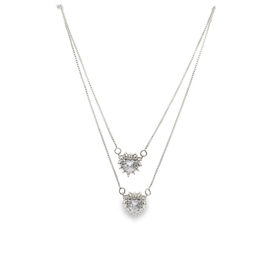 A delicate double-layered silver necklace features two sparkling heart-shaped crystal pendants against a clean white background.