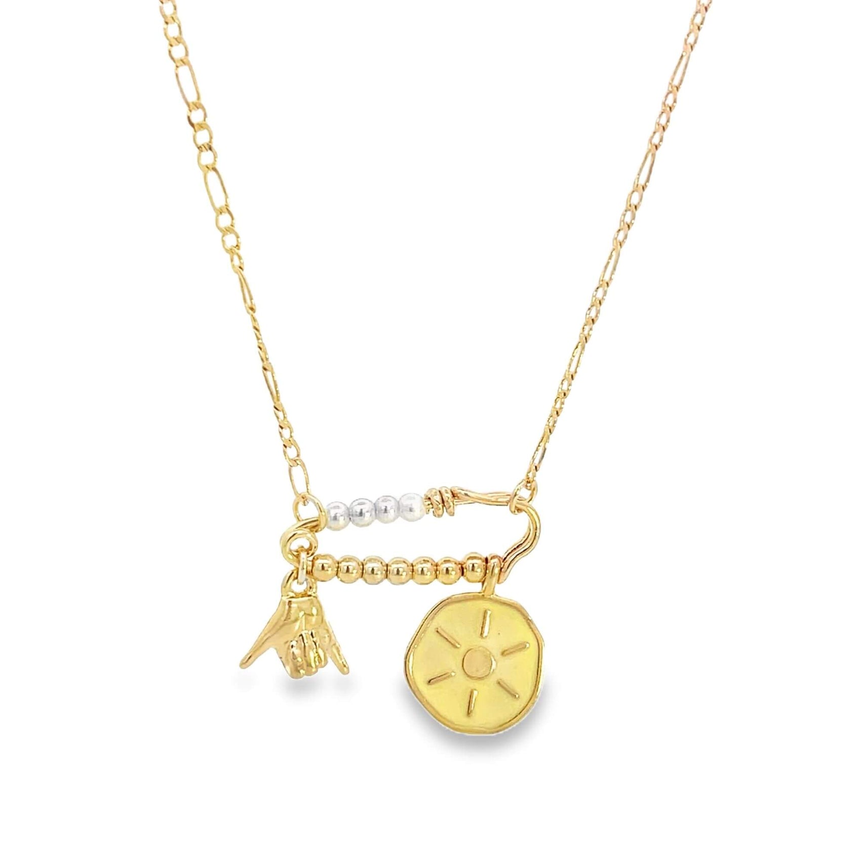 A delicate gold chain necklace features a safety pin pendant embellished with beads and charms, including a hand sign and a sun medallion.