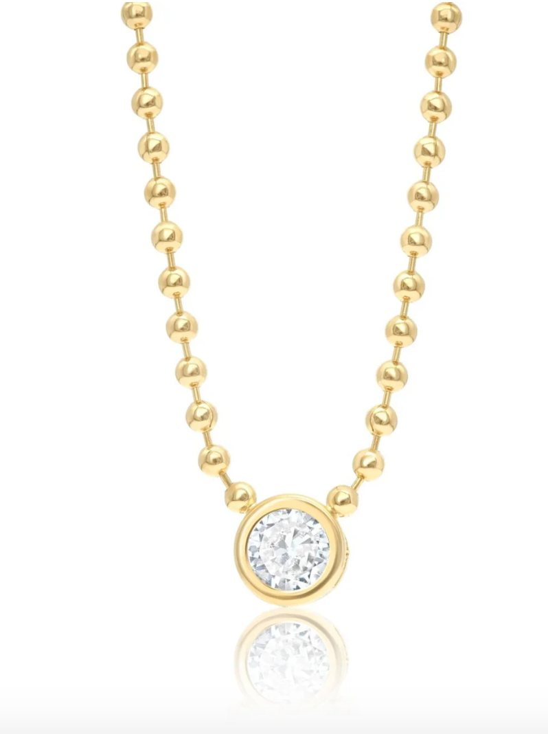 A gold beaded chain necklace showcases a round, bezel-set diamond pendant hanging in the center.