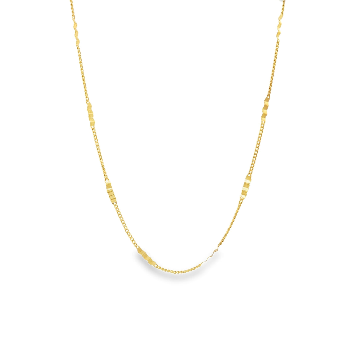 A delicate gold chain necklace with evenly spaced patterned links curves against a white background.