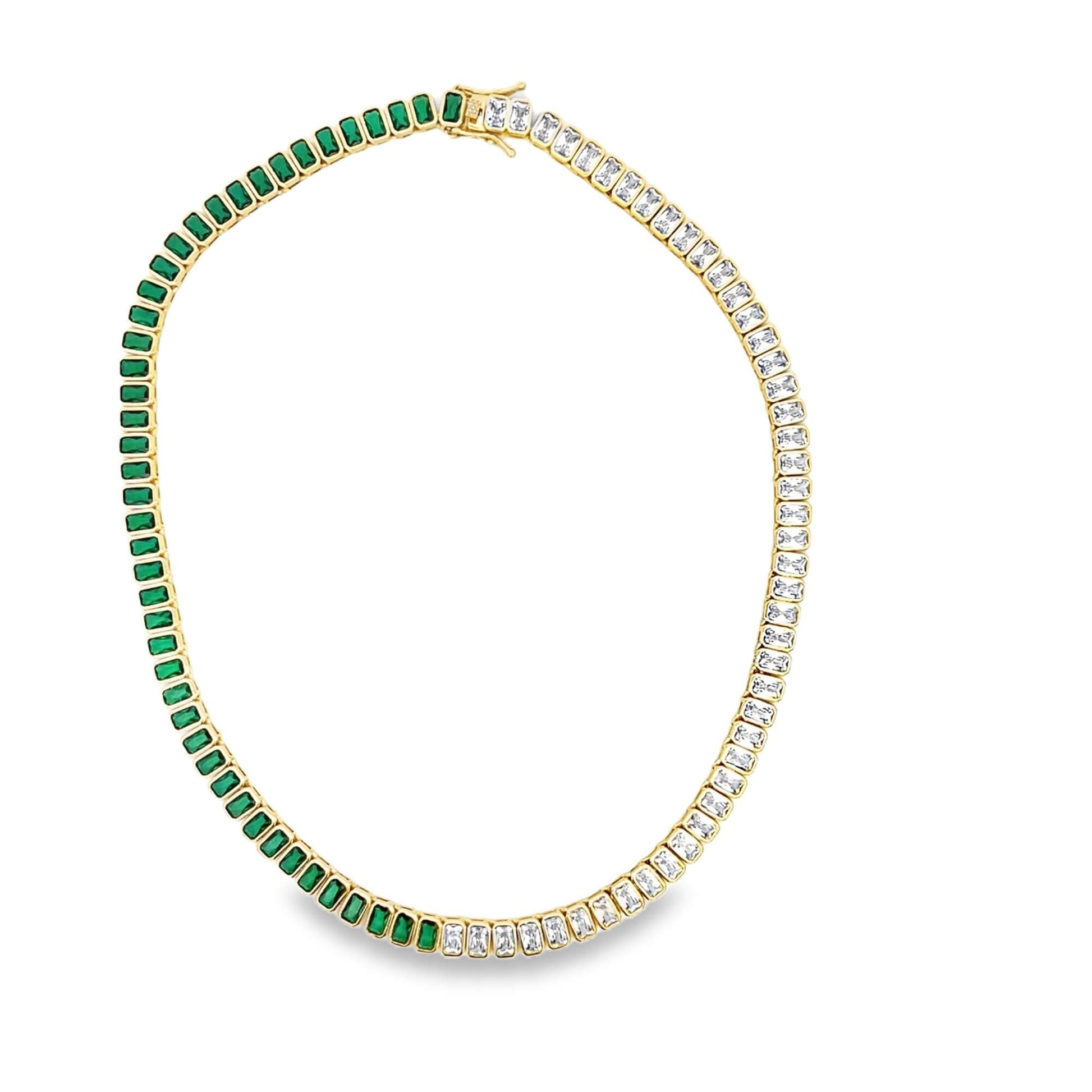 A gold tennis necklace features alternating emerald-cut green and white gemstones arranged in a continuous loop against a white background.