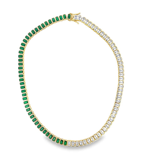 A gold tennis necklace features alternating emerald-cut green and white gemstones arranged in a continuous loop against a white background.