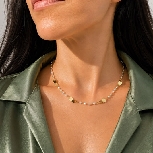 A woman wearing a gold chain necklace with interspersed pearls and flat gold discs poses in a green silk shirt.