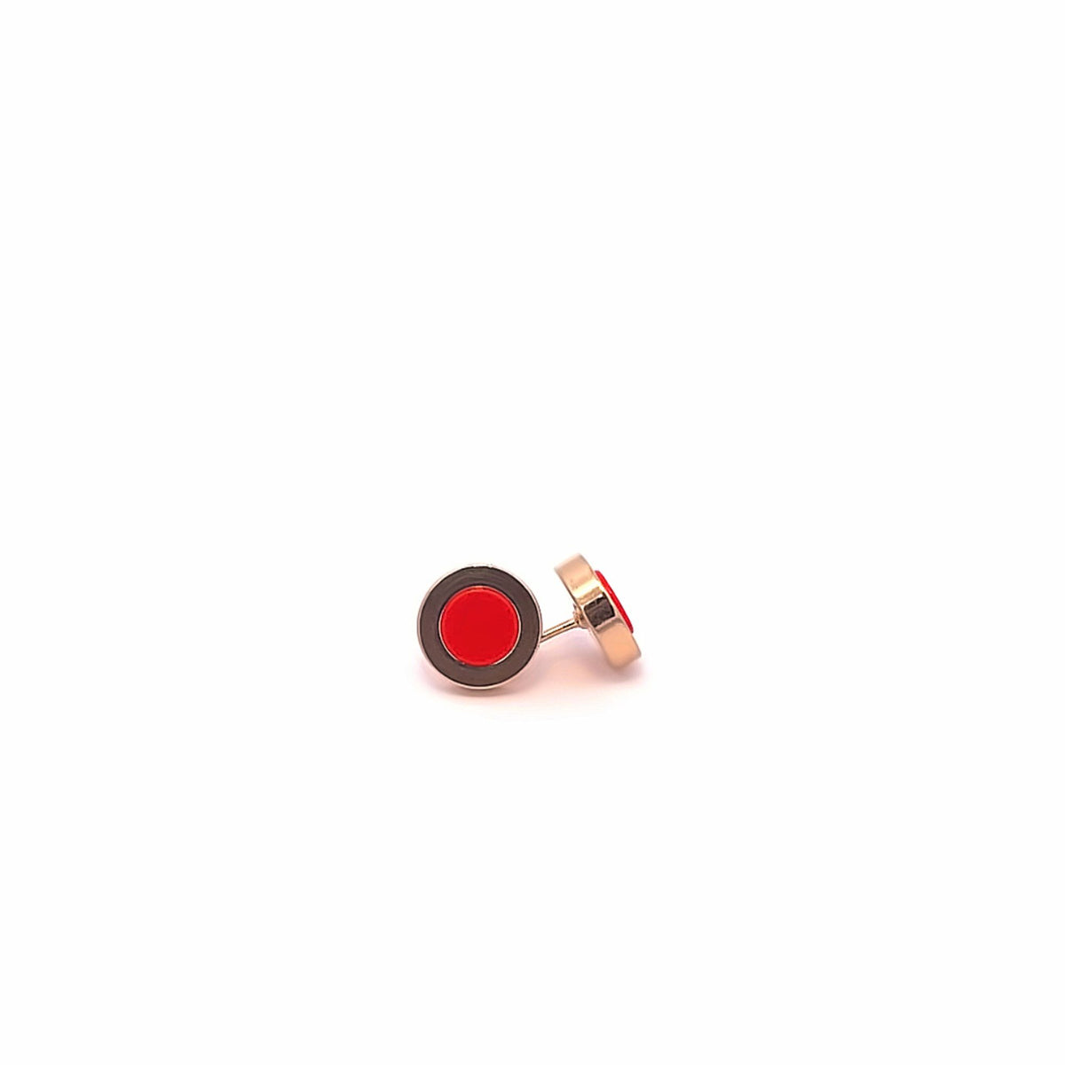A pair of minimalist round stud earrings featuring vibrant red centers framed by black enamel rest on a clean white surface.