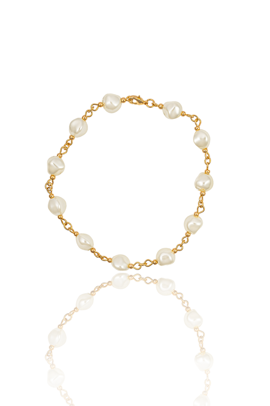 A delicate gold chain bracelet features baroque pearls and rests against a white background with a subtle reflection.