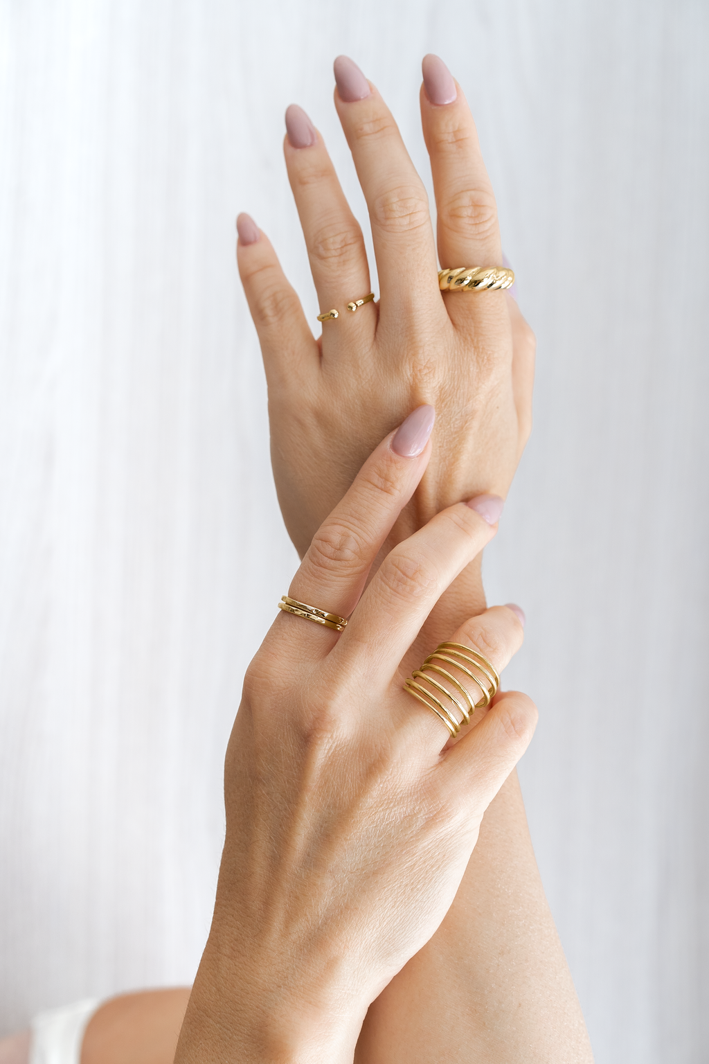 A woman showcases a collection of elegant gold rings on her fingers against a bright, textured background.
