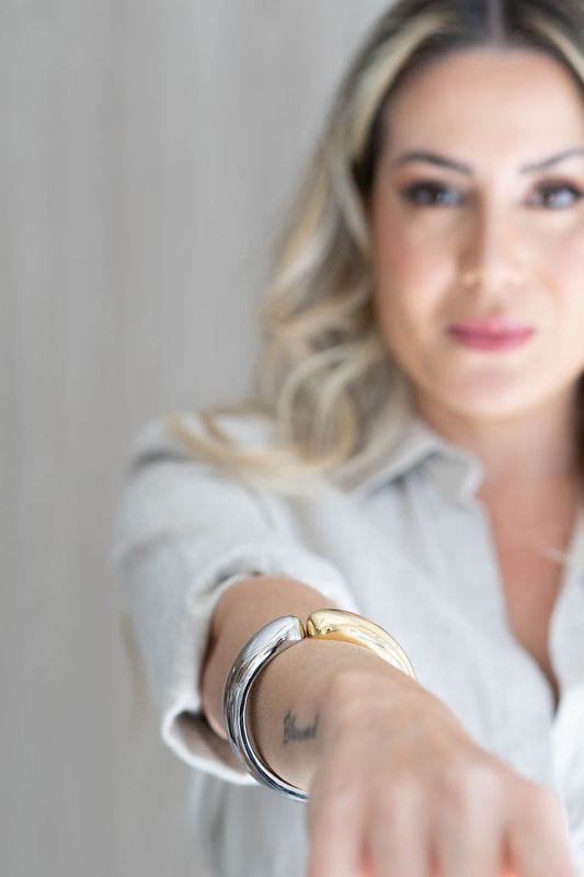 A woman showcases a thick two-toned gold and silver metal cuff bracelet on her wrist.