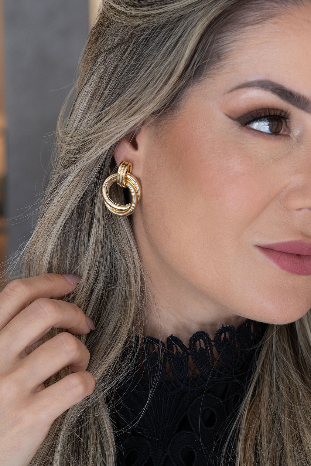 A blonde woman wearing elegant gold interlocking circle earrings poses for a close-up portrait.