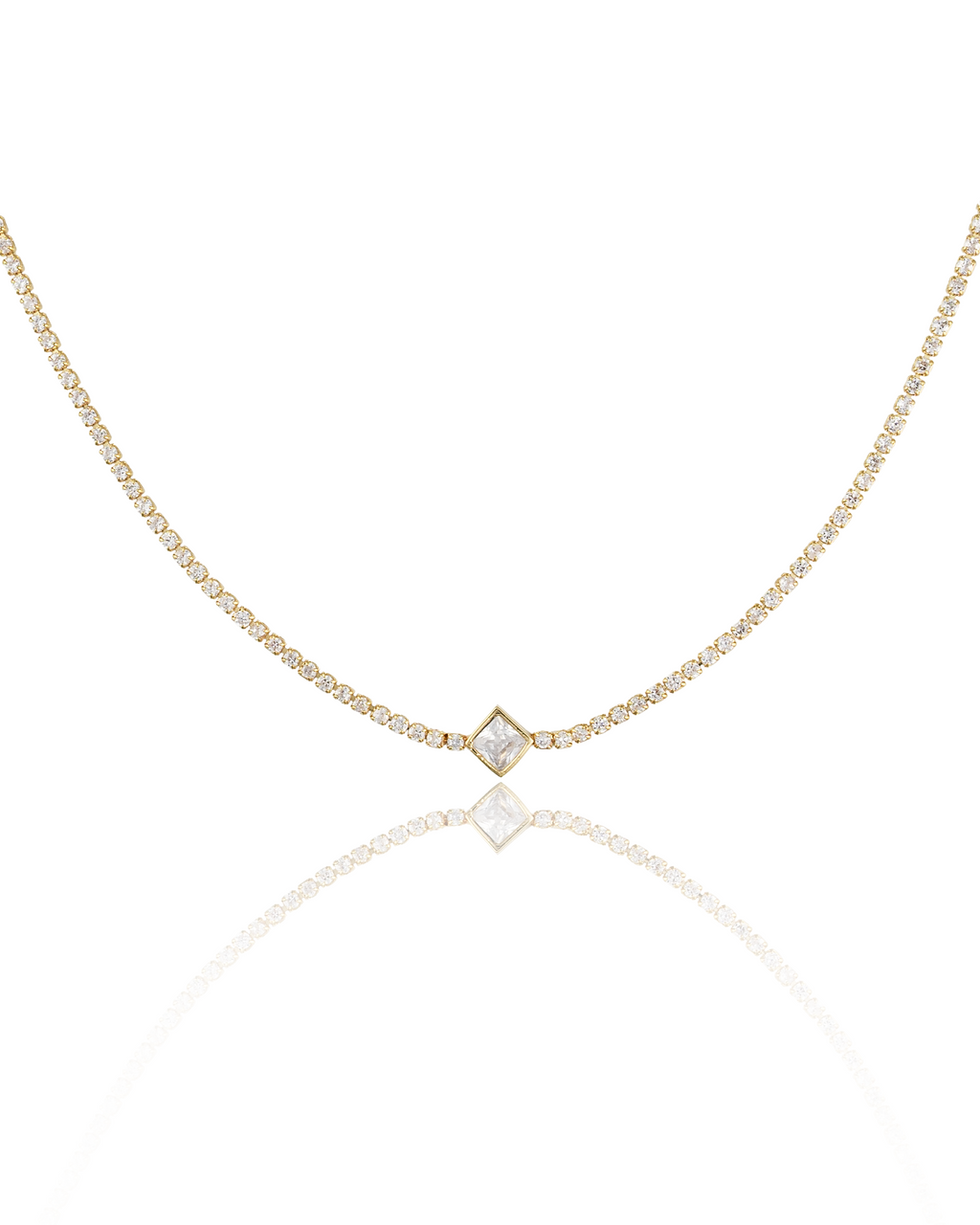 A delicate gold diamond tennis necklace featuring a square-cut pendant rests on a reflective white surface, displaying its sparkling stones.