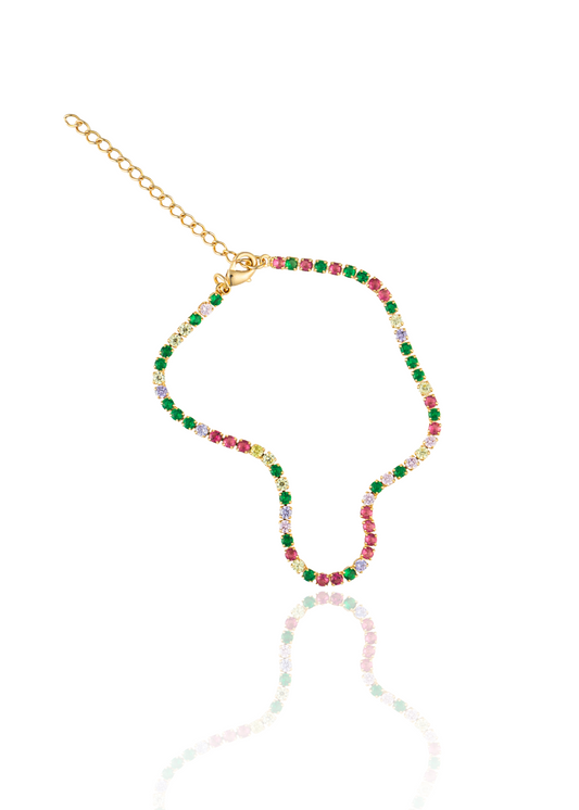 A gold tennis necklace featuring vibrant multi-colored cubic zirconia stones lies on a white reflective surface.