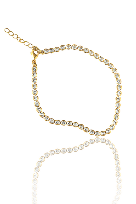 A glittering gold tennis bracelet set with sparkling diamonds lies on a reflective white surface.