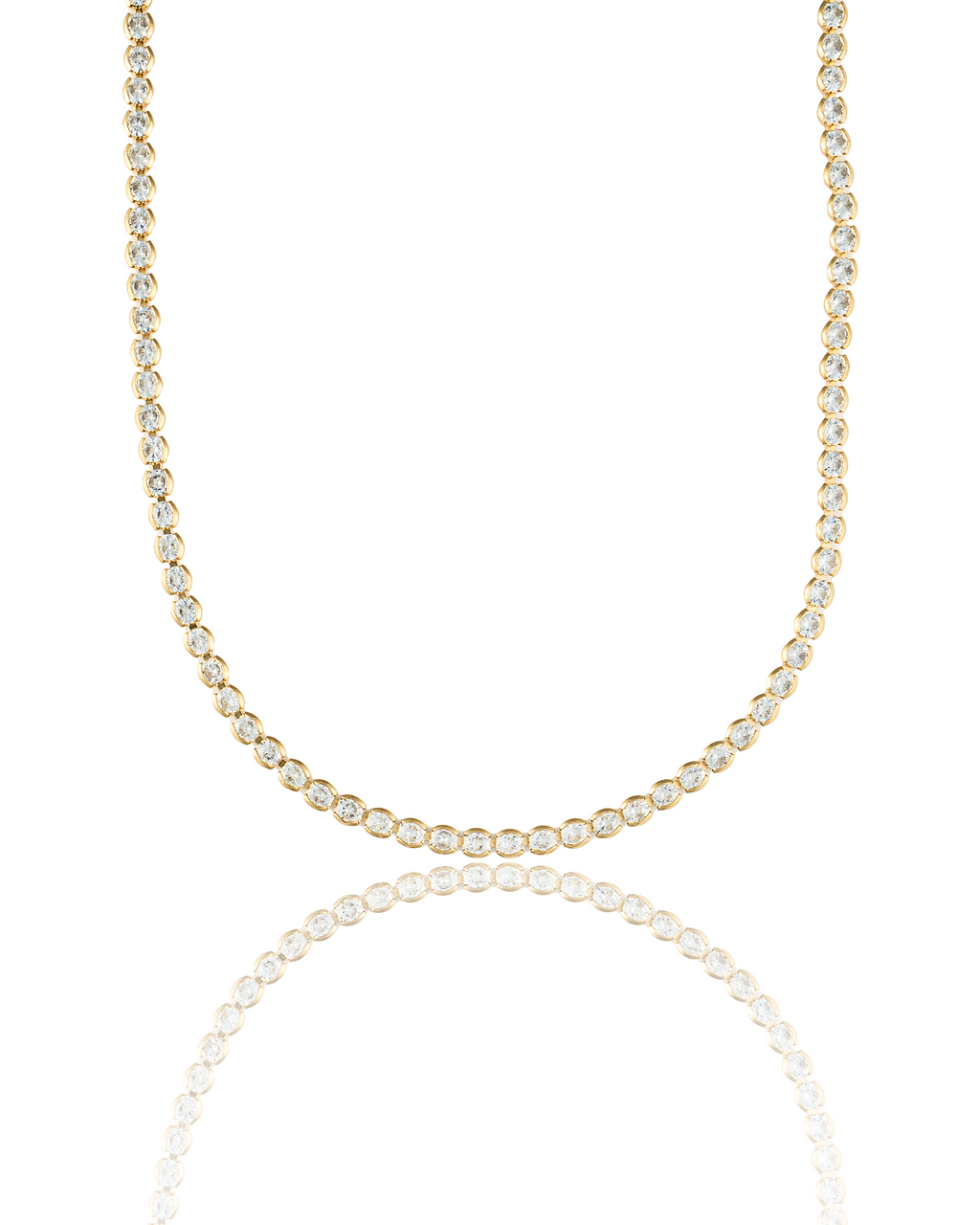 A sparkling diamond tennis necklace rests on a reflective white surface against a clean background.