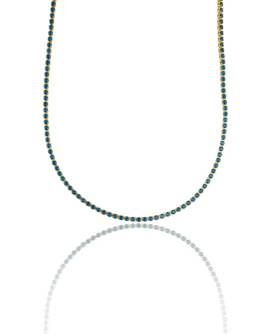 A gold tennis necklace featuring vibrant blue stones curves gracefully against a white background with a subtle reflection below.