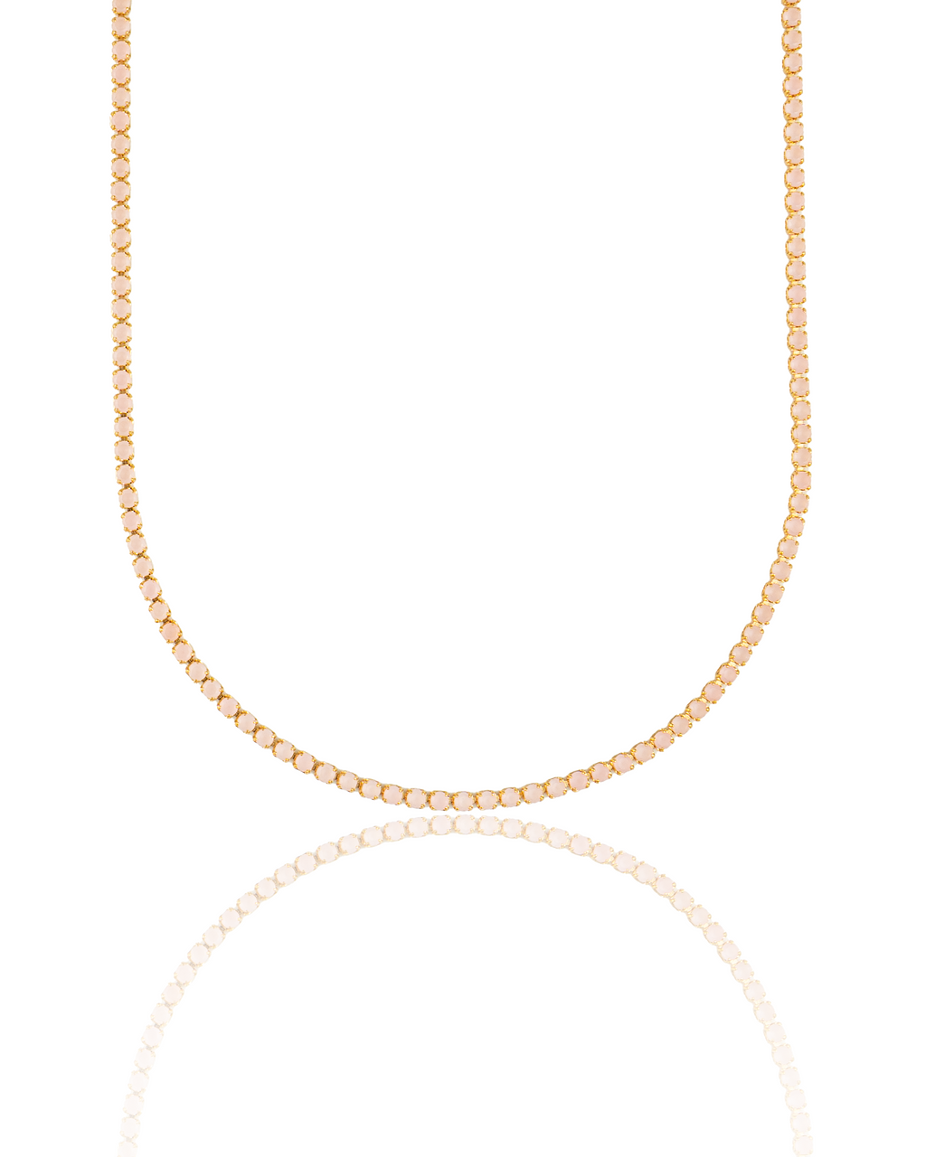 A delicate gold tennis necklace featuring sparkling pale pink stones hangs against a clean white background, reflecting softly below.