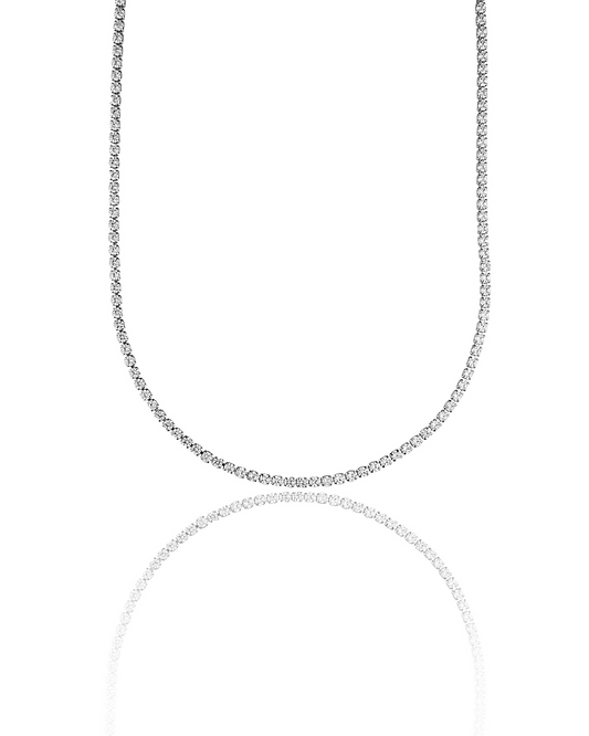 A gleaming diamond tennis necklace hangs in a graceful curve against a clean white background, reflecting softly below.