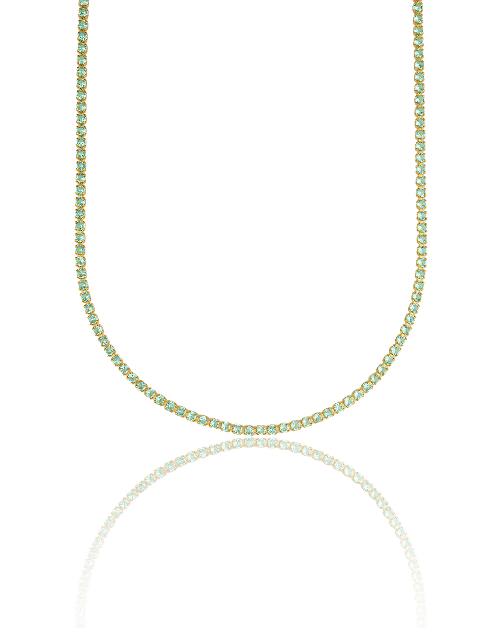 A sparkling gold tennis necklace studded with continuous light green gemstones hangs against a clean white background with its reflection visible below.