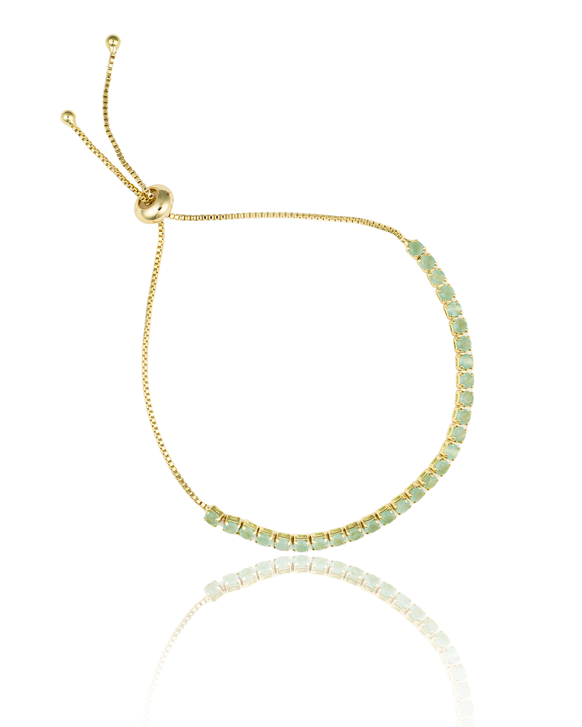 A delicate gold bolo tennis bracelet features a curved line of small, round green stones and an adjustable sliding closure.