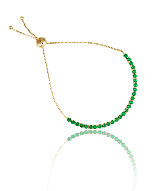 A delicate gold adjustable bolo bracelet sparkles with vibrant green cubic zirconia stones against a white background.